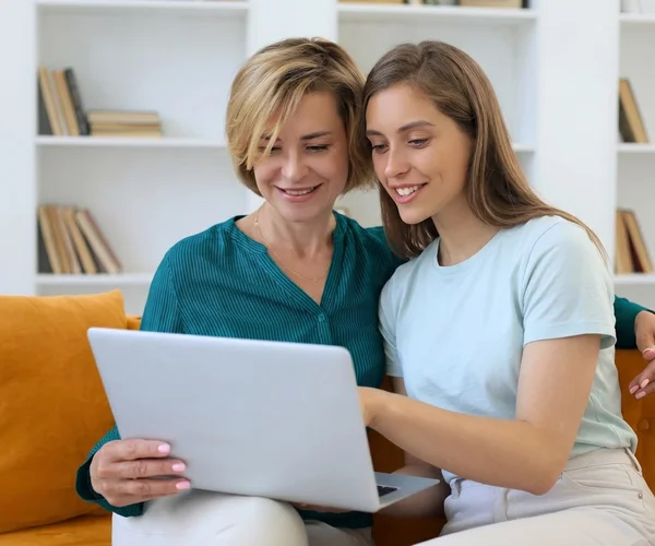 A parent and student sitting on a couch, smiling while looking at a laptop together